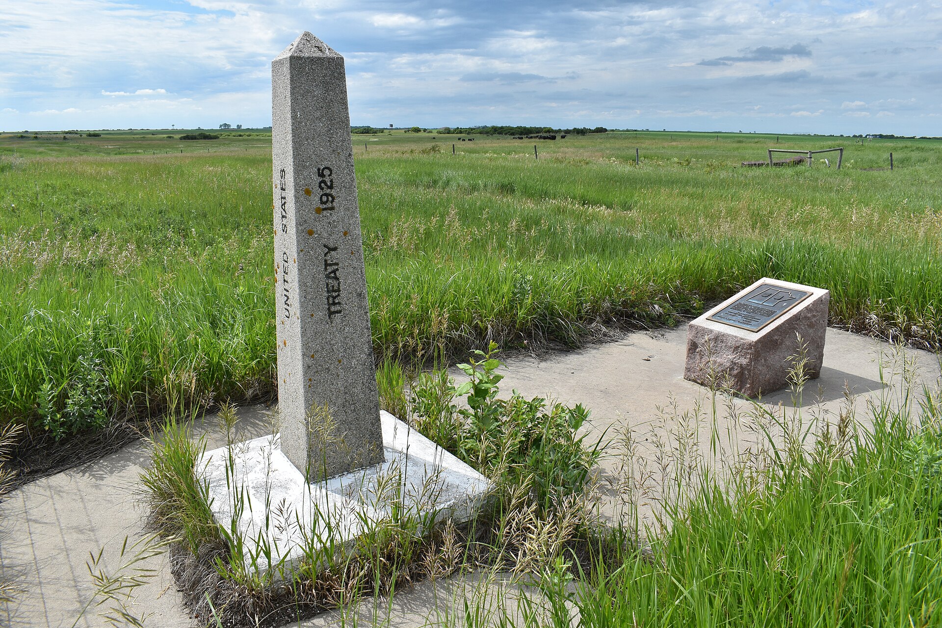 A stone obelisk and plaque in tall prairie grass under a wide sky.