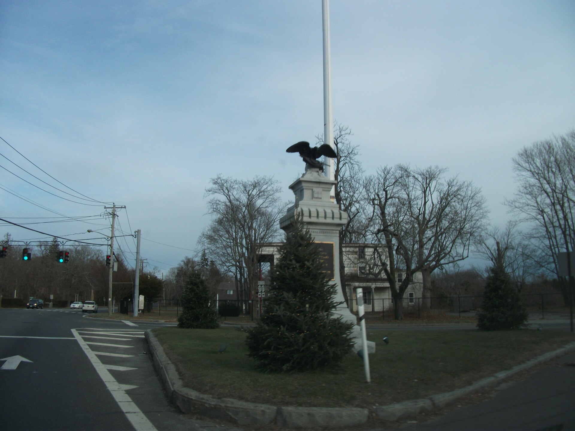 A stone monument topped with an eagle at a village intersection with evergreen trees.