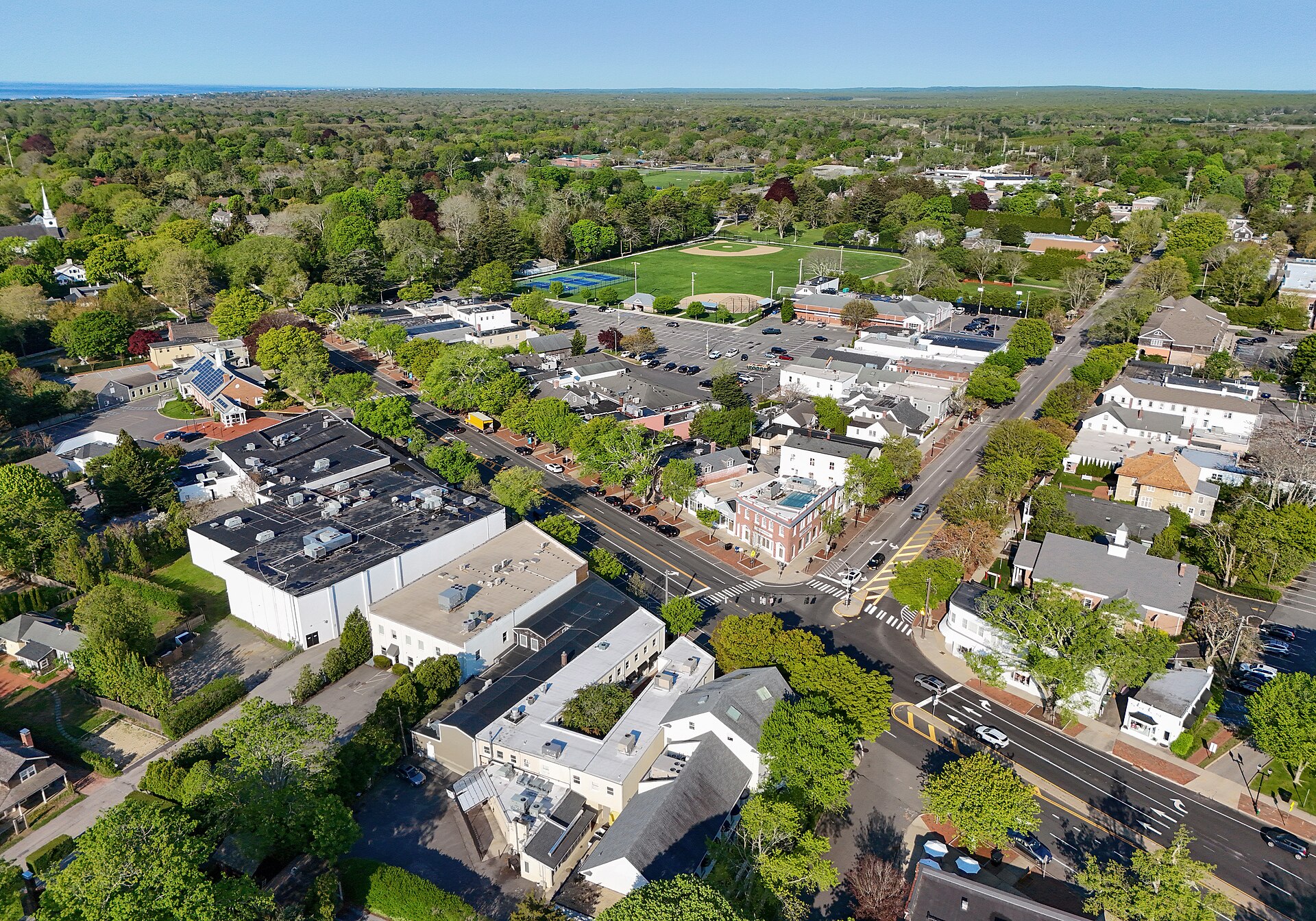 A drone view over the village's rooftops, churches, and green fields with the ocean beyond.