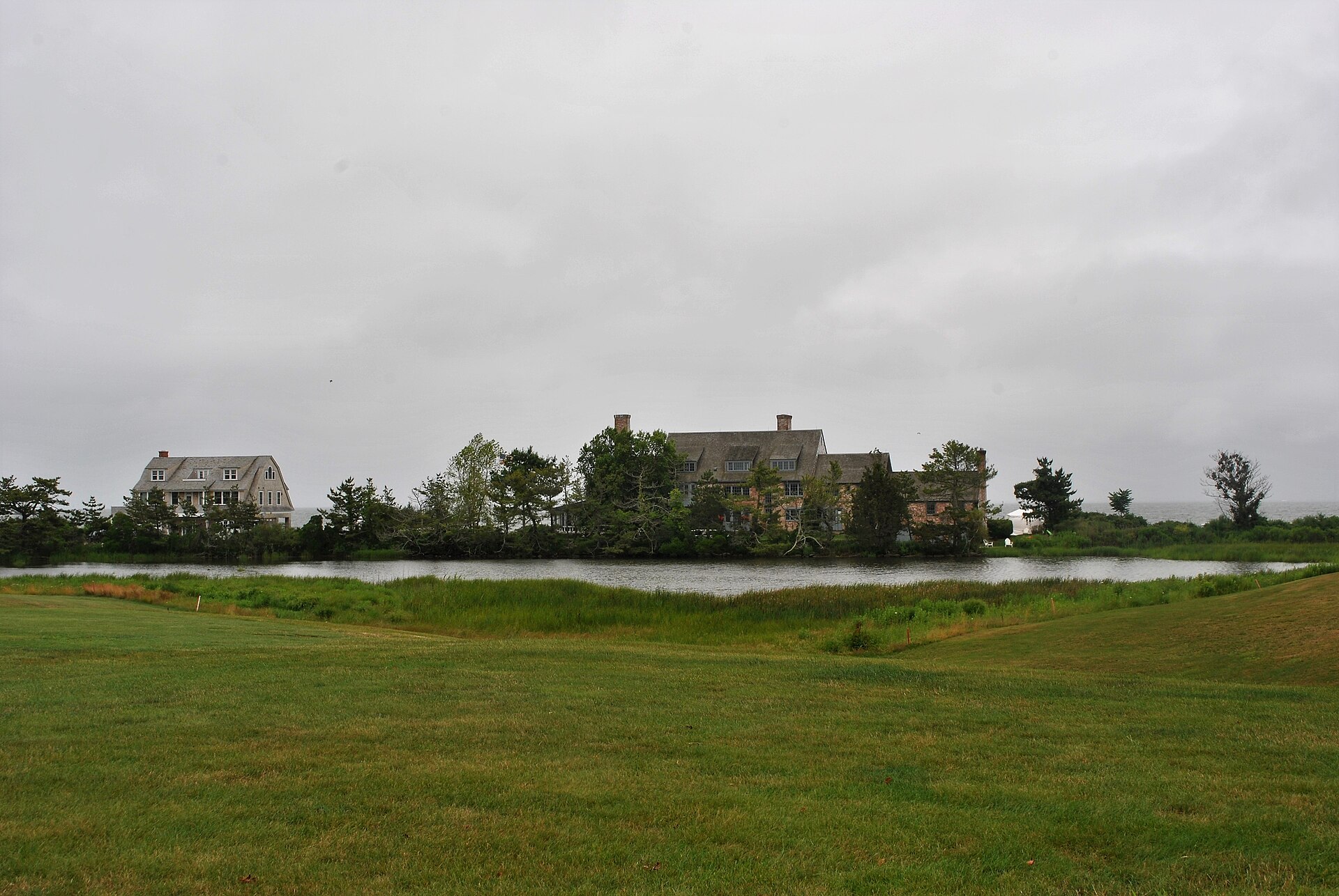 A large shingled house on the water in Fenwick, seen across a lawn on an overcast day.