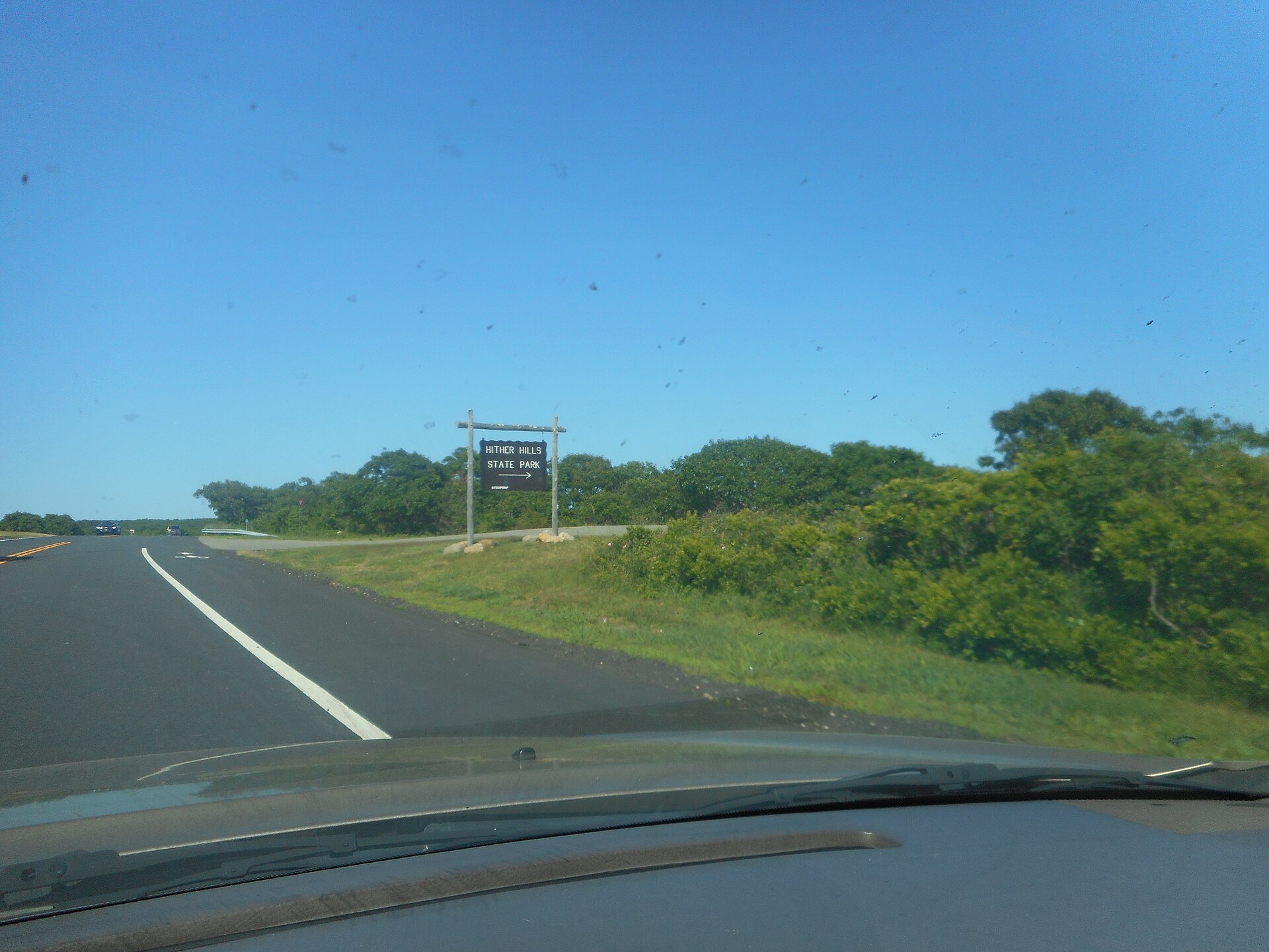 A wooden park sign beside a highway with dense green woods beyond.