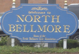 A blue sign reading Welcome to North Bellmore beside a road.