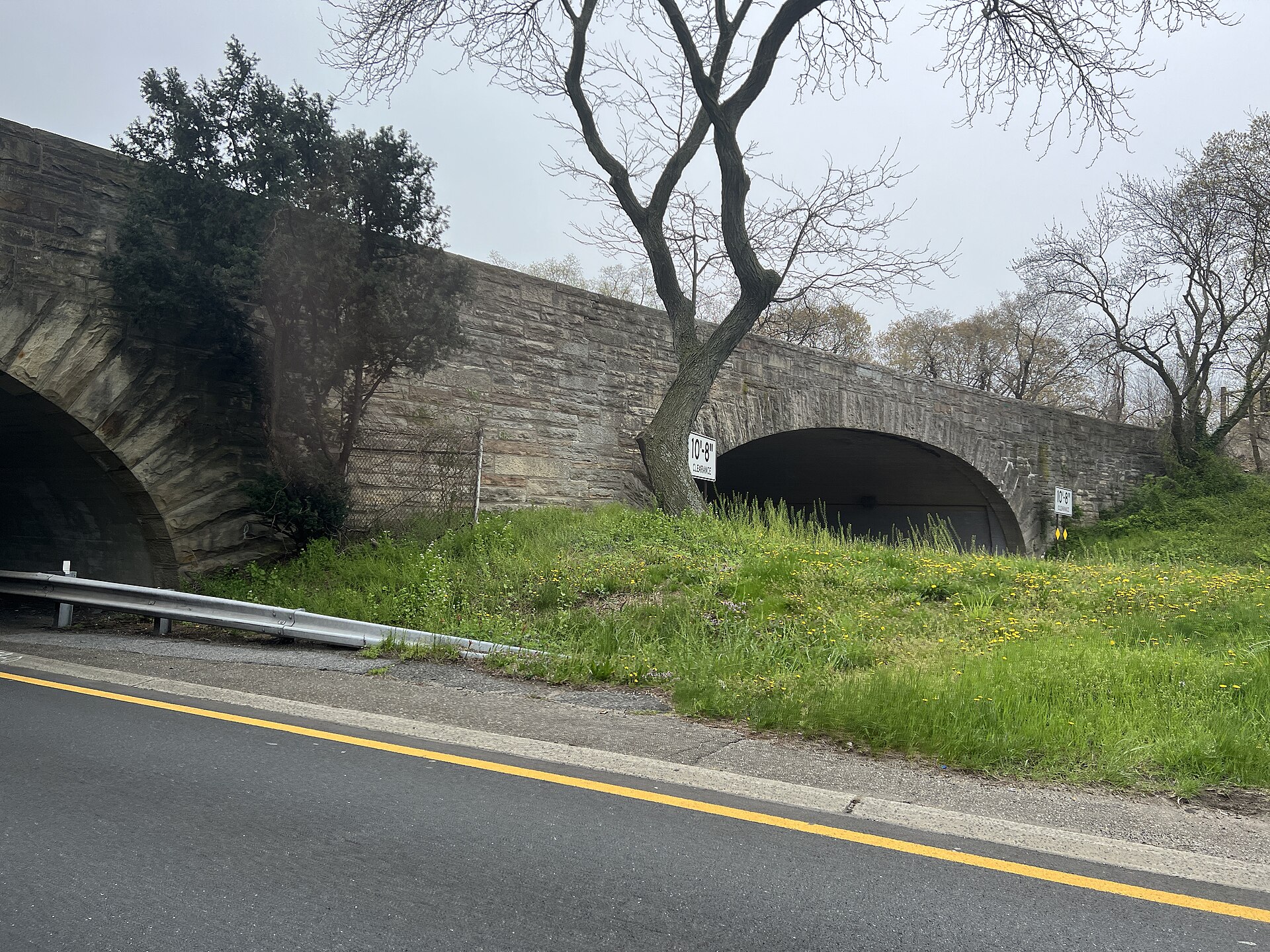 A stone arch bridge carrying a road over a multi-lane parkway with grassy embankments.