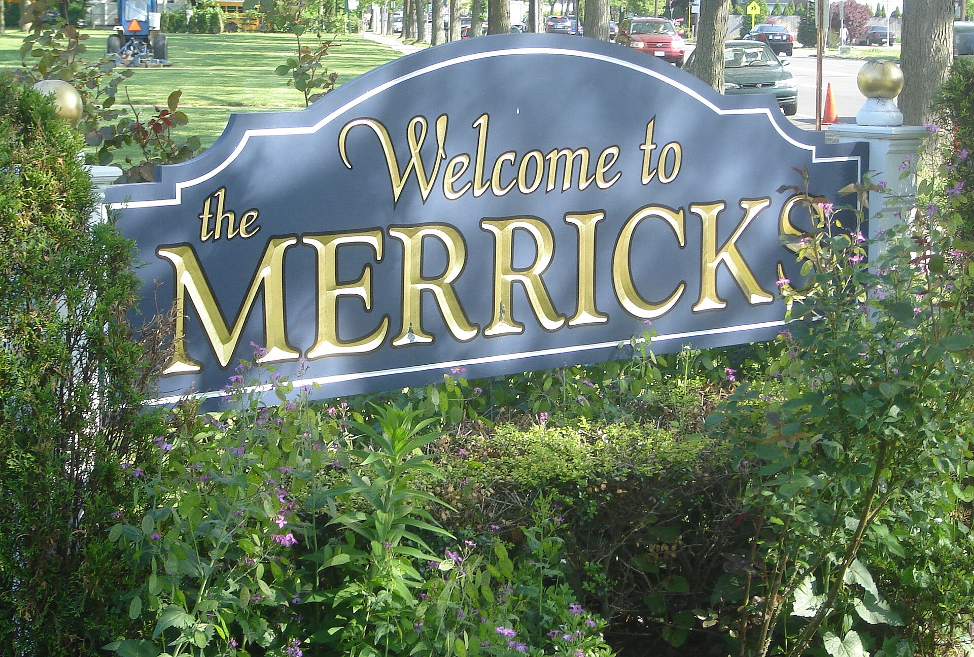 A blue and gold 'Welcome to the Merricks' sign surrounded by greenery.