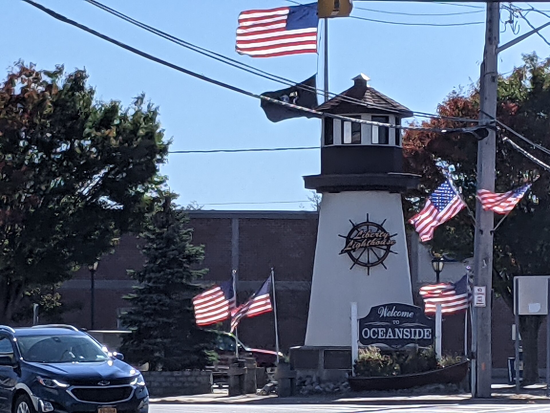 A clock tower monument welcoming visitors to Oceanside New York with American flags.