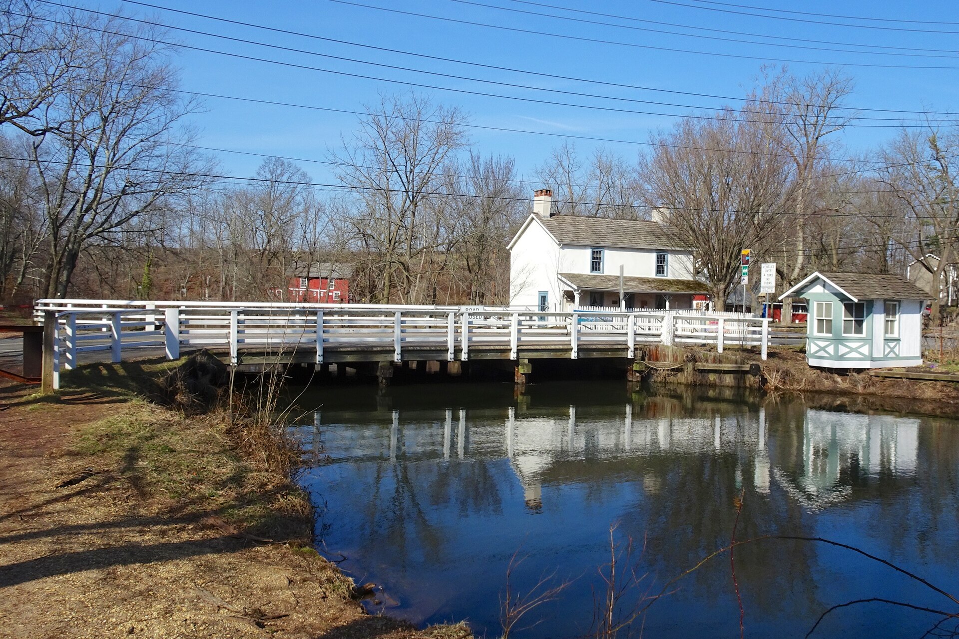 A white bridge tender's house beside a canal bridge in Blackwells Mills, New Jersey, with the water reflecting the scene.