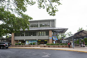 A modern two-story train station building with a parking lot in front.