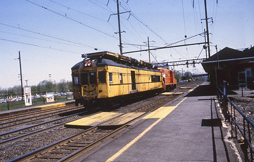 A yellow maintenance train stopped at a station platform under overhead wires.