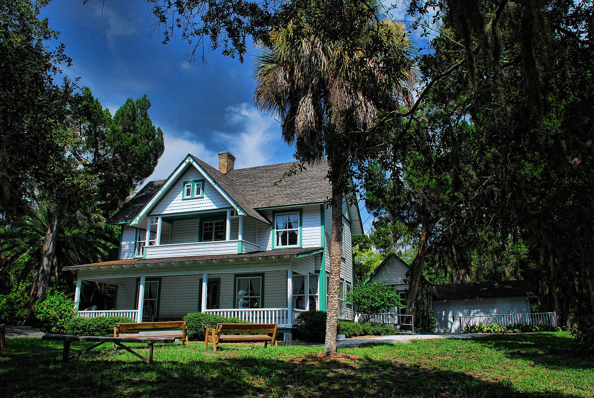 A historic two-story house with a wraparound porch and palm trees at Spanish Point in Osprey, Florida.