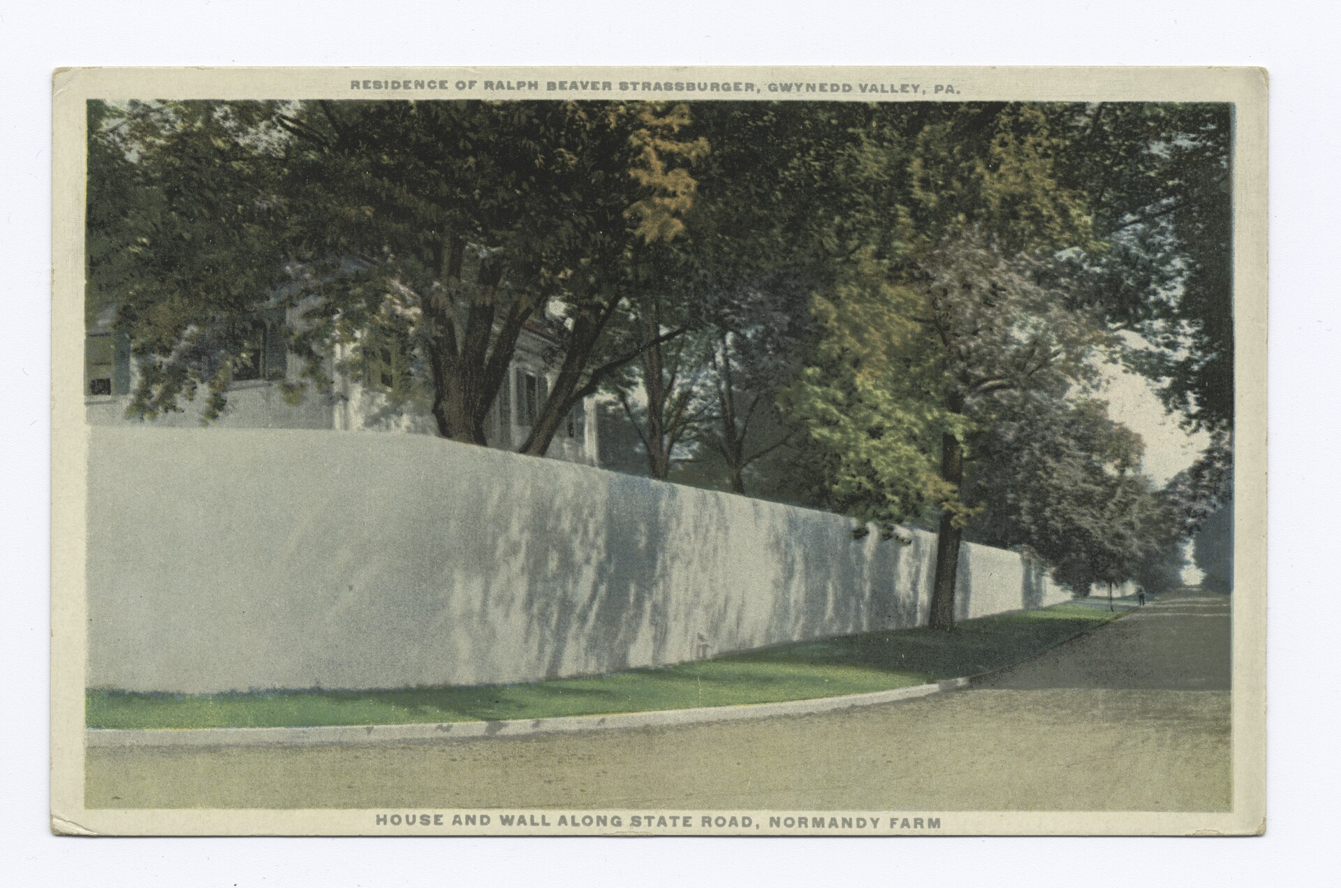 Sepia historic photo of a large house and long wall along a road.