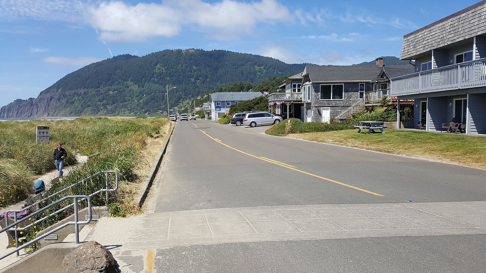 A quiet street in Manzanita, Oregon, lined with beach houses, with a forested mountain rising in the distance.