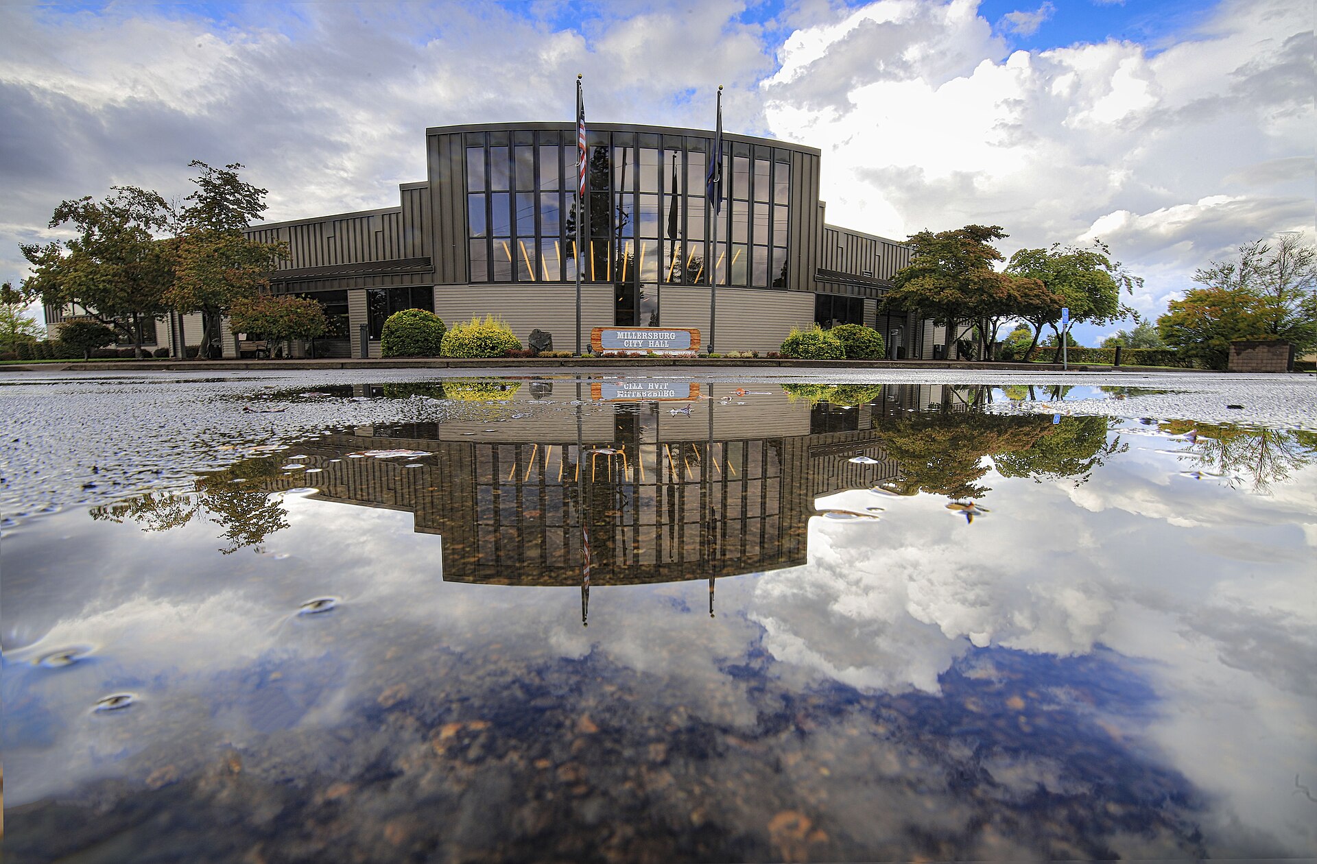The modern Millersburg city hall building reflected in a pool of water.