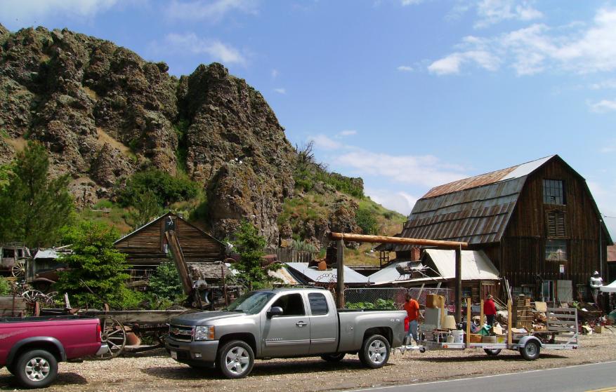 A wooden barn museum with vintage trucks parked outside against a rocky hillside.