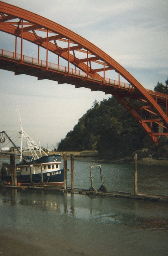 The orange Rainbow Bridge over the water in La Conner Washington with a boat passing under.