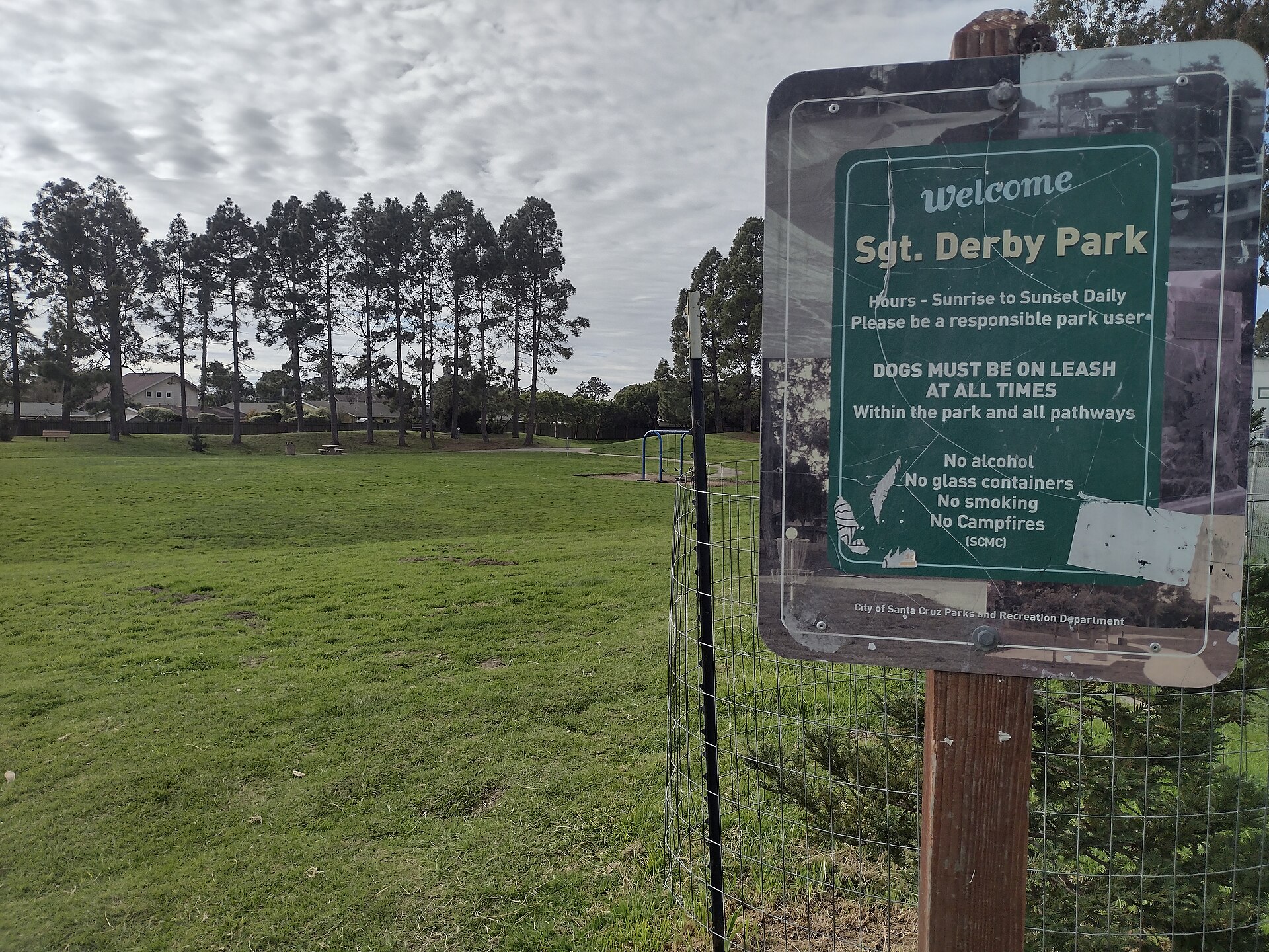 The welcome sign for Sgt. Derby Park in Santa Cruz with a green lawn and tall trees behind it.