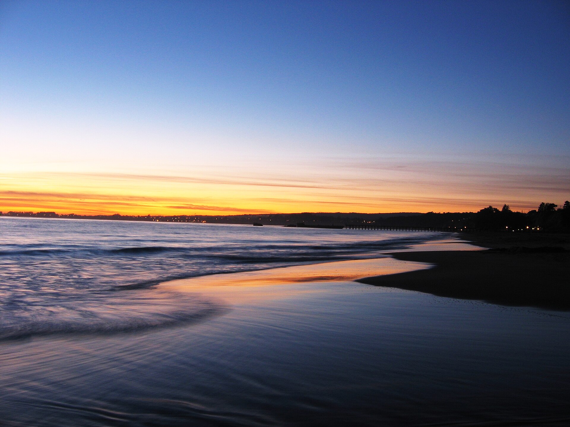 Sunset over the Pacific at Seacliff Beach with orange light reflecting on the wet sand.