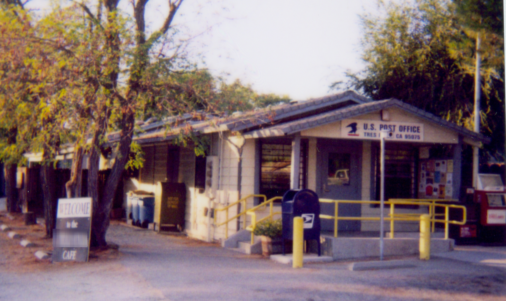 The U.S. Post Office in Tres Pinos, a small building with a blue mailbox and yellow railings out front.