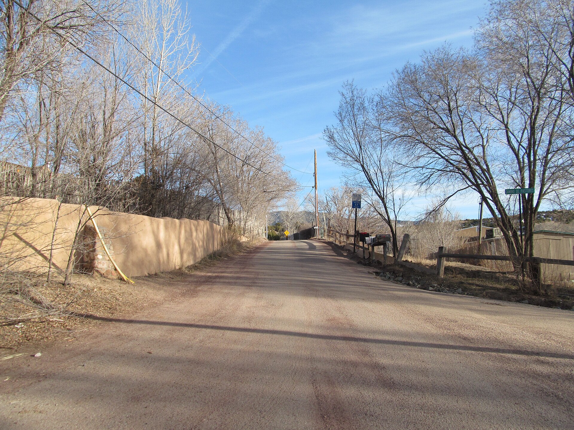 A quiet dirt road in Chupadero, New Mexico lined with adobe walls and bare winter trees.