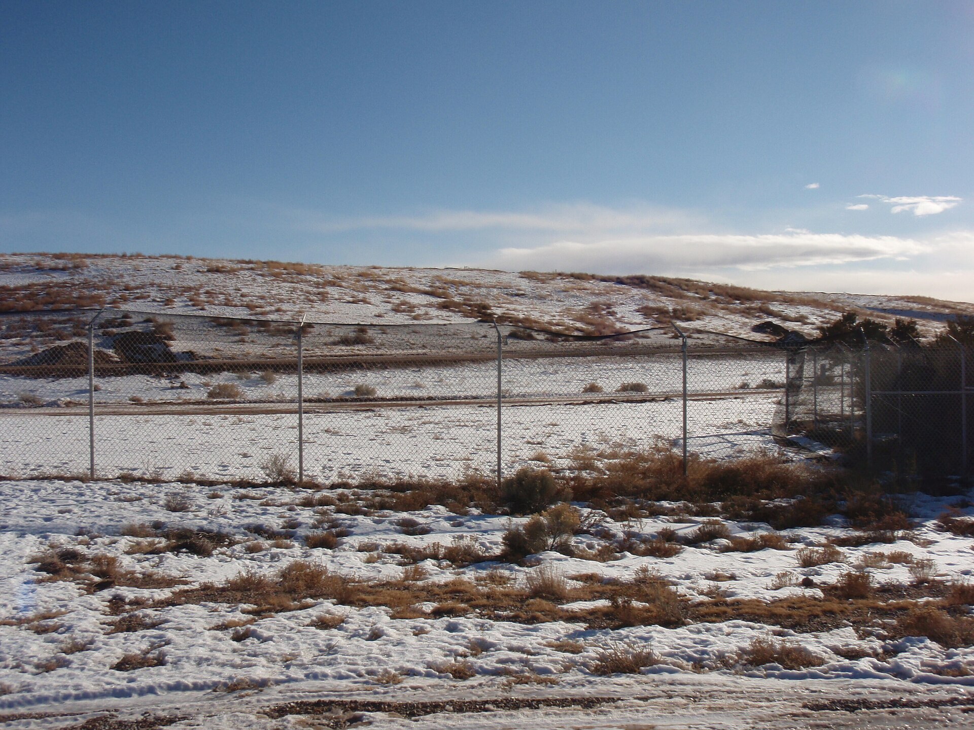 A light snowfall over a fenced field in La Tierra with a snow-dusted mesa behind.