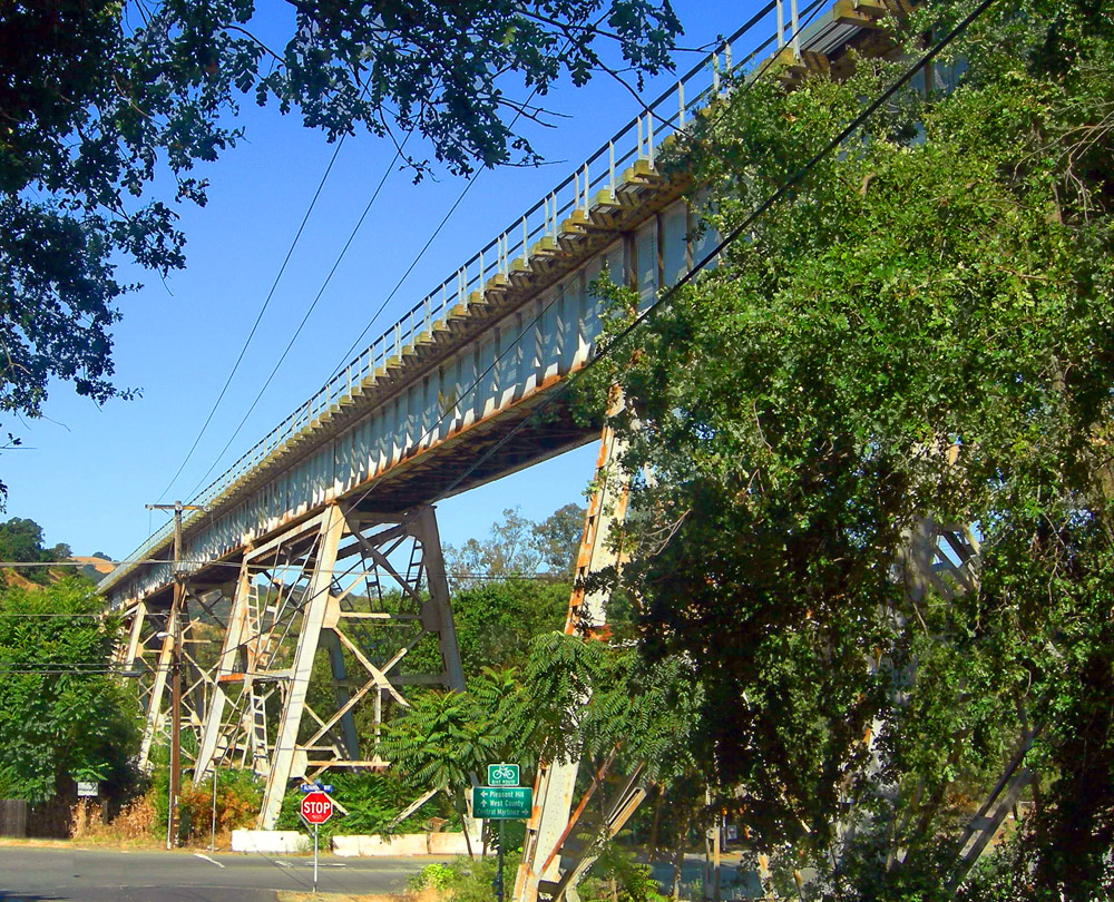 A steel railroad trestle bridge arching over a road in Alhambra Valley.