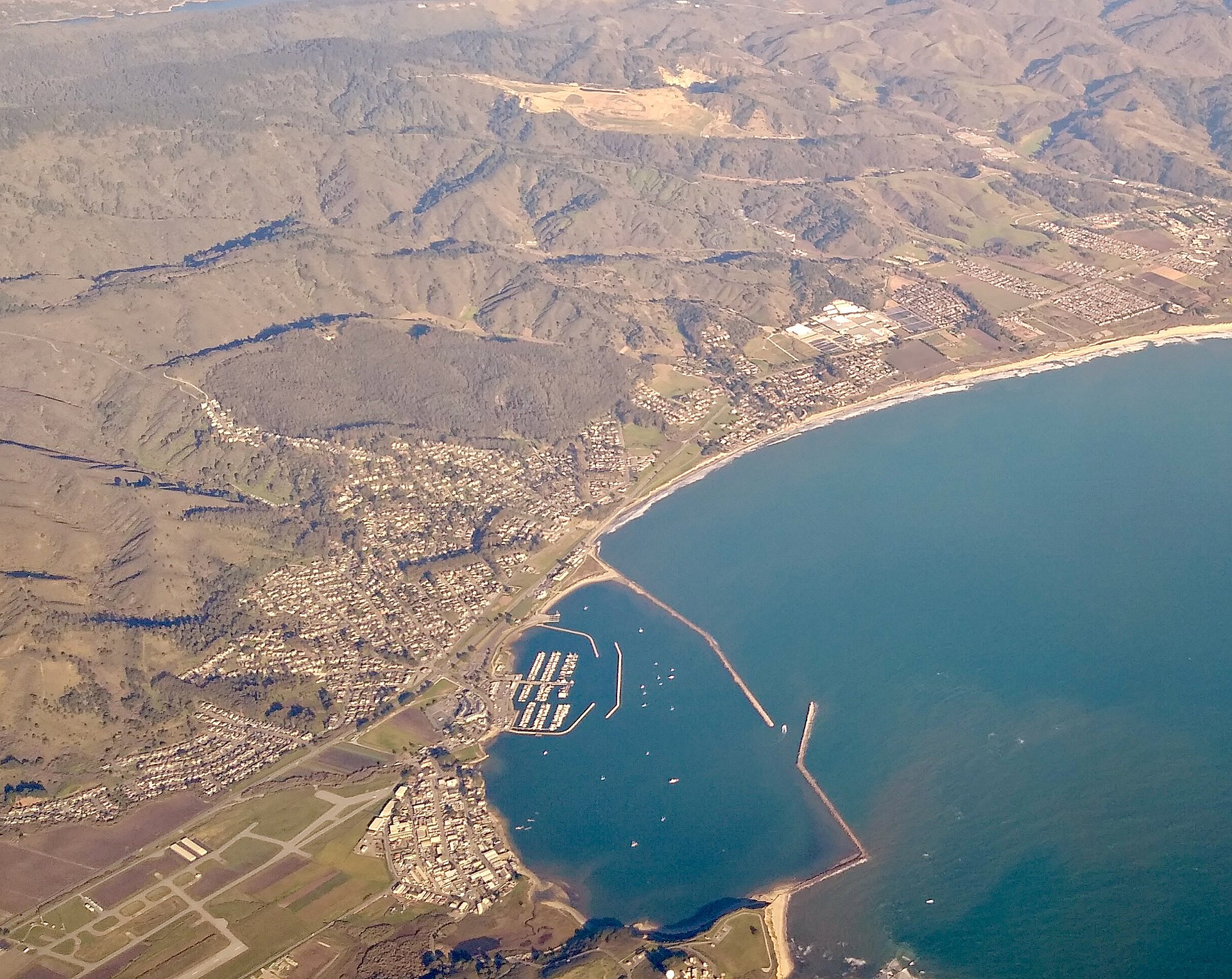 Aerial view of Pillar Point Harbor at El Granada, with boats moored in the marina and the Half Moon Bay breakwater curving into the bay.