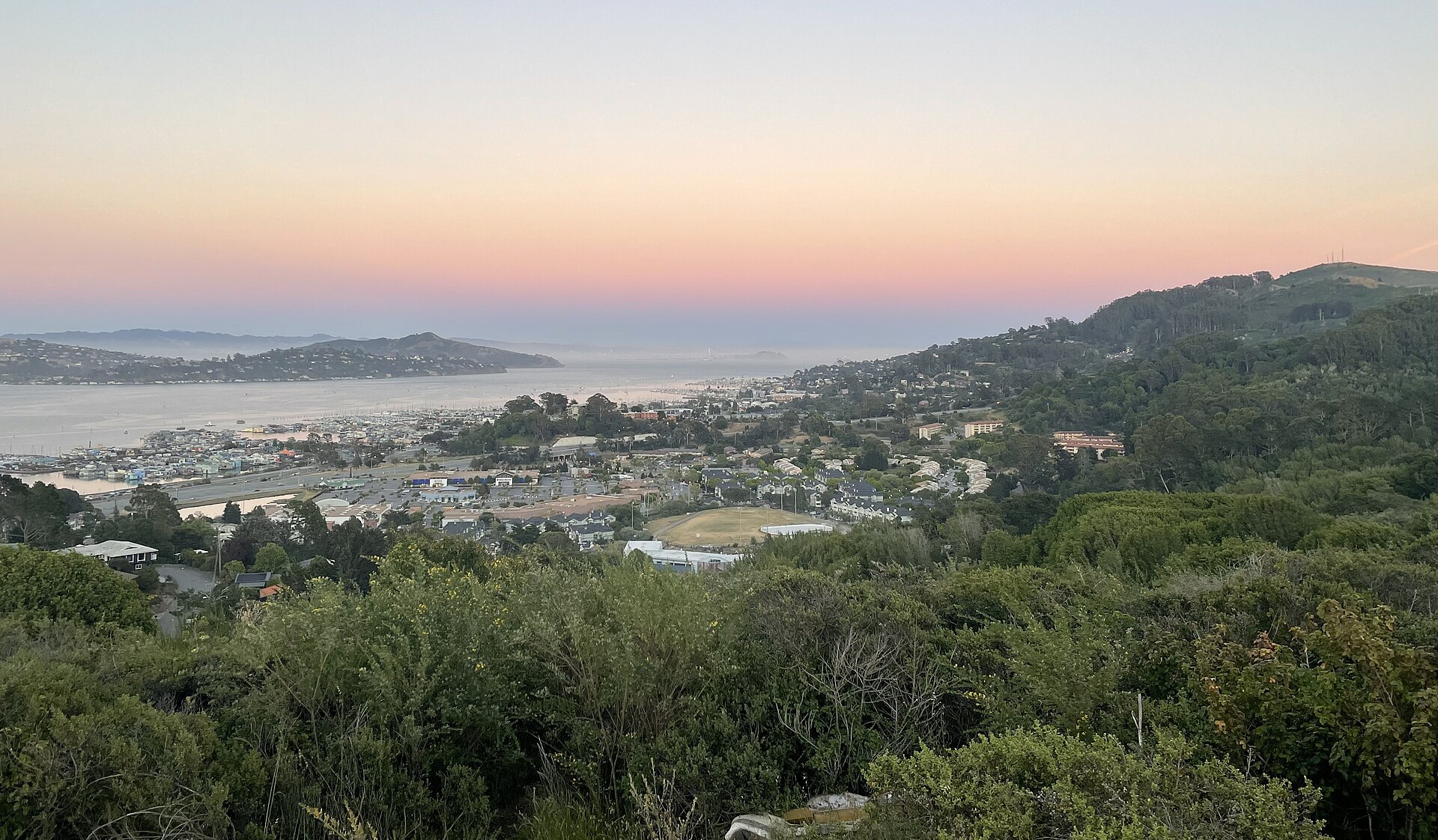 Sunset view over Marin City from the Alta Trail, with the town nestled between green hills and the bay beyond.