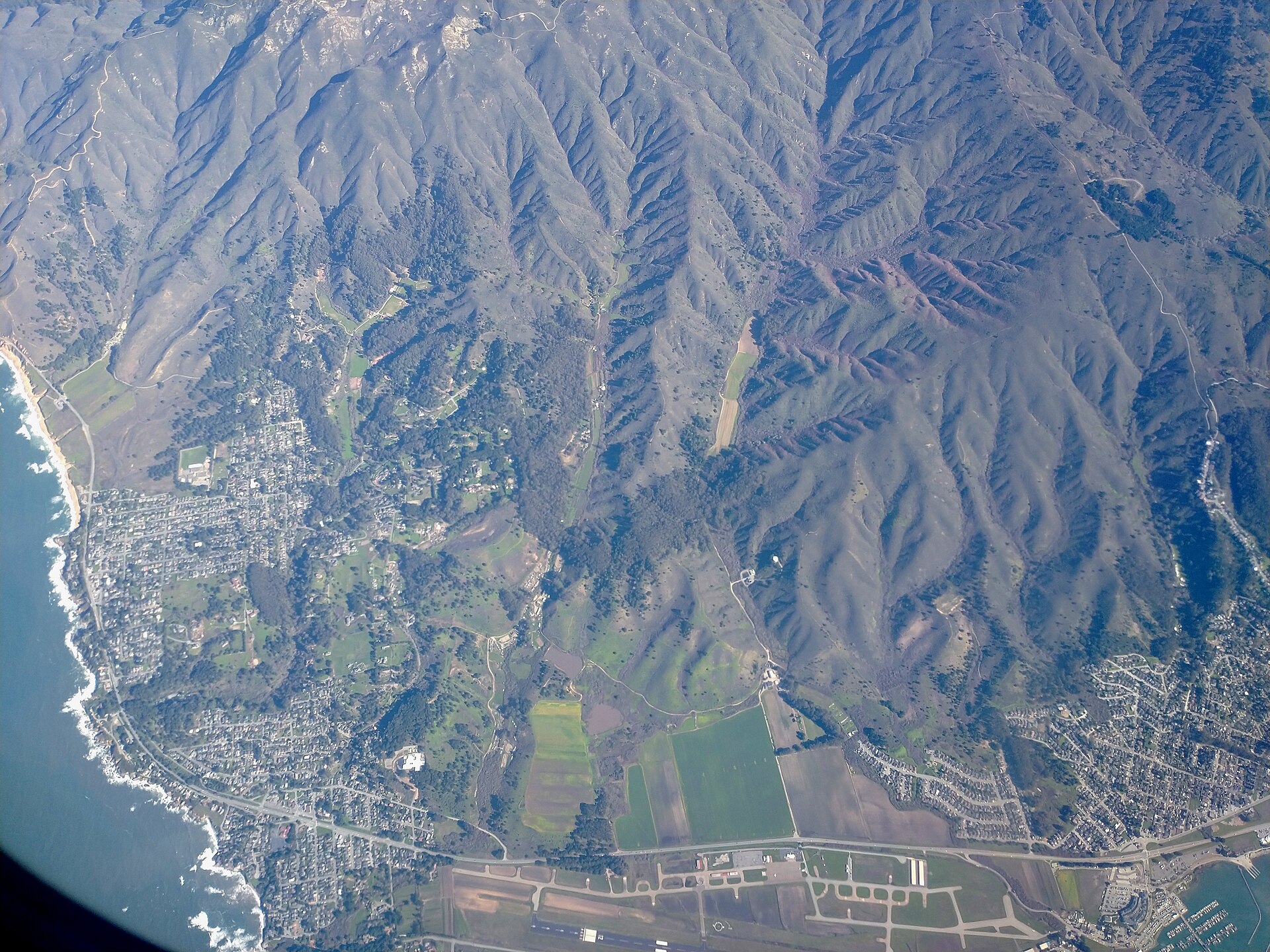 Aerial view of the Moss Beach coastline, with the town tucked between the ocean and the coastal mountains.