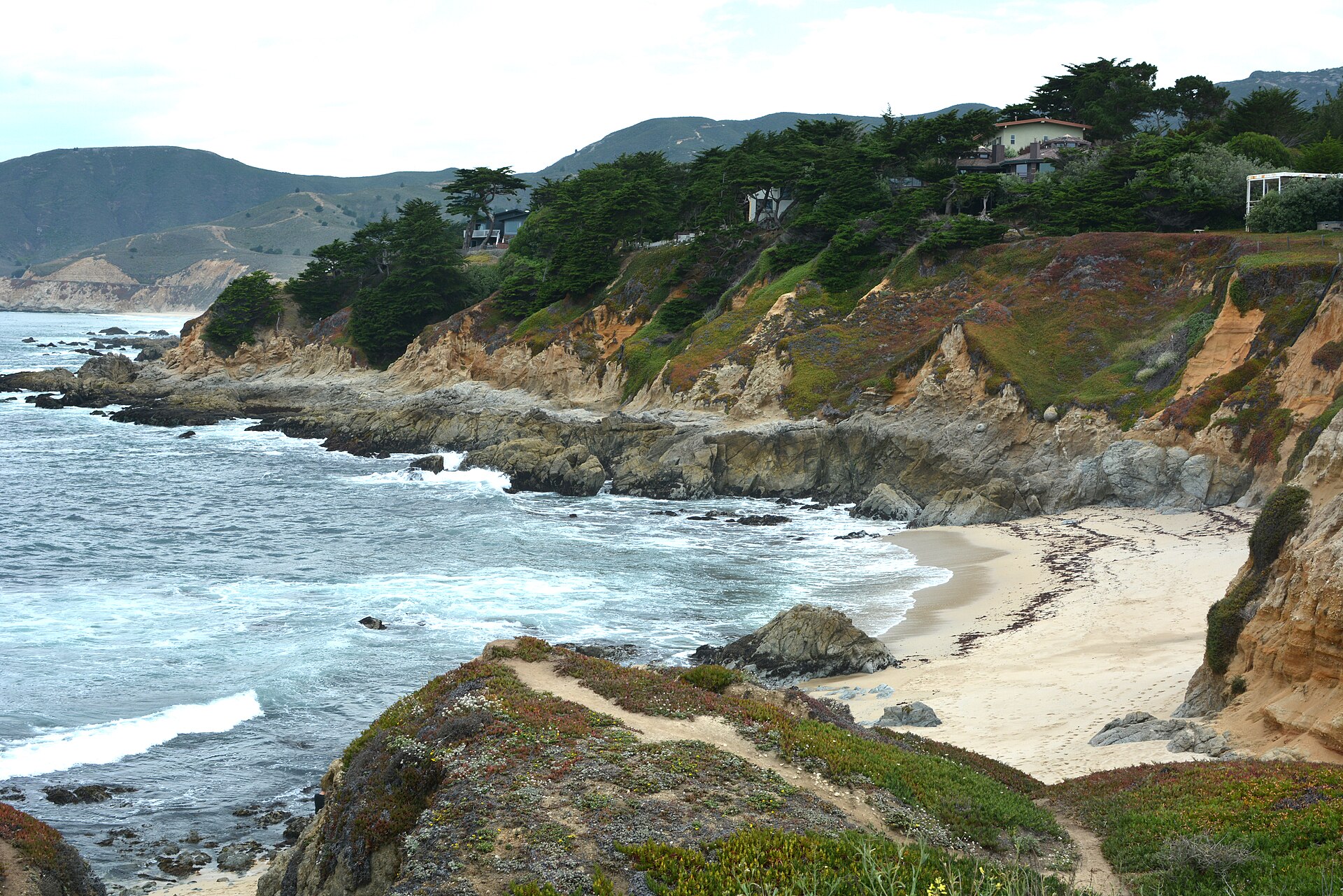 A rocky cove at Moss Beach with waves breaking on the shore and houses on the cliffs above.