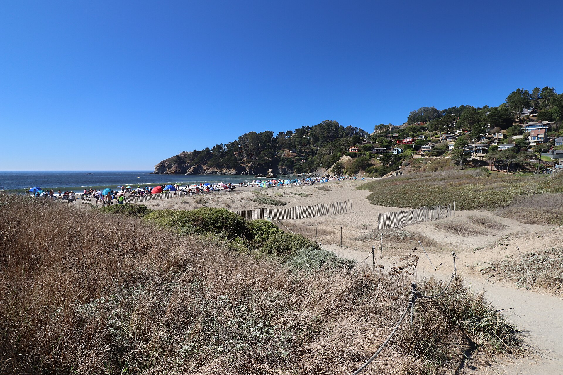 Muir Beach on a busy day, with visitors spread across the sand and the coastal hills rising behind.