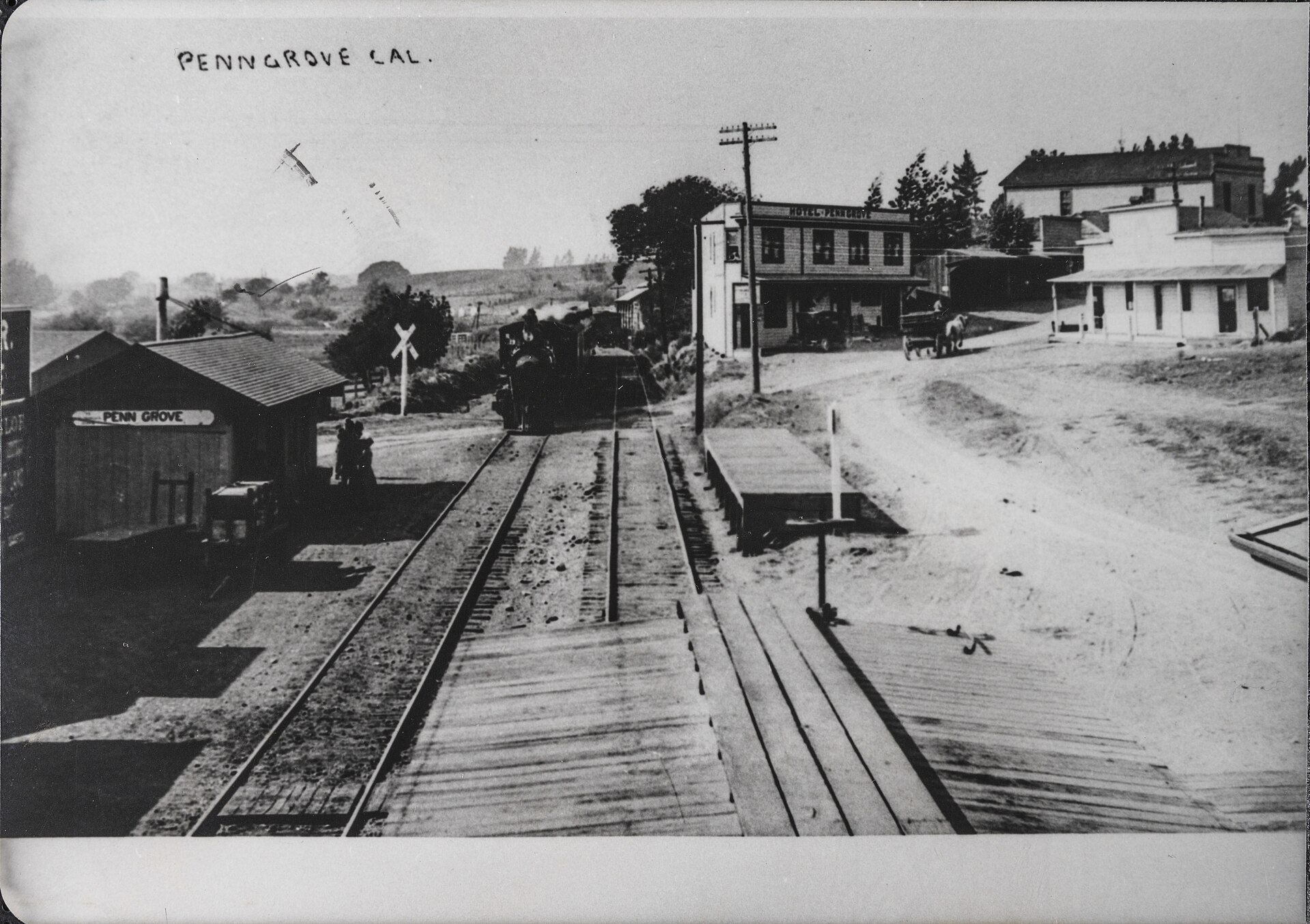A historic photograph of Penngrove's railroad station with tracks, a depot, and storefronts labeled 'Penngrove Cal'.