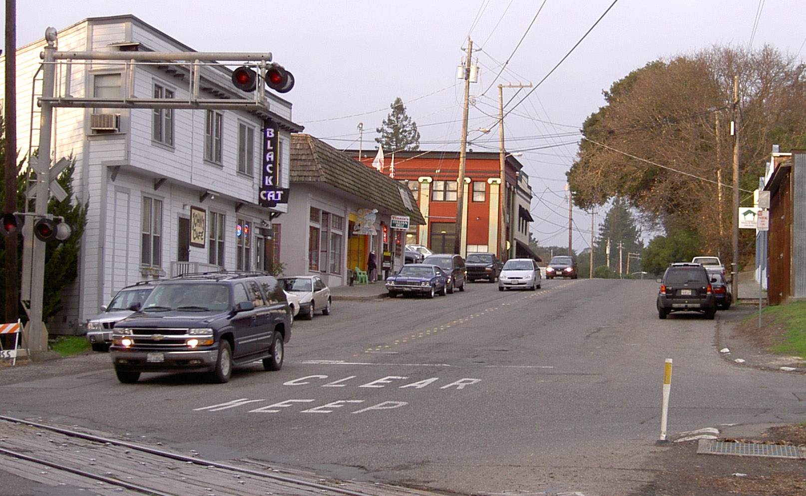 Main Street in Penngrove with storefronts, parked cars, and railroad crossing signals.