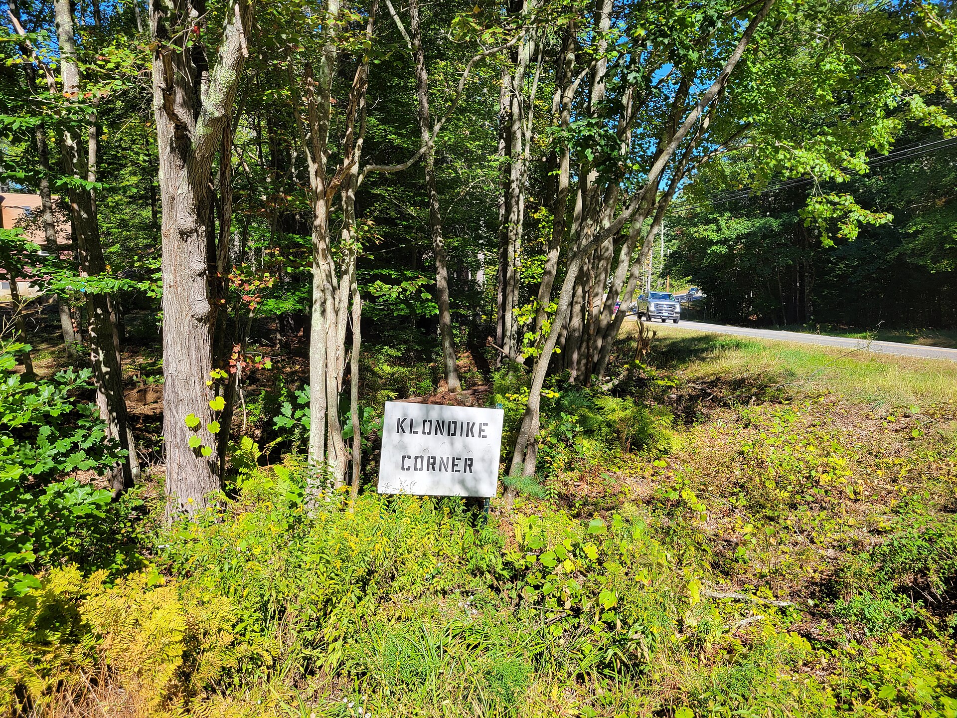 A small Klondike Corner sign among trees and brush in New Boston, New Hampshire.