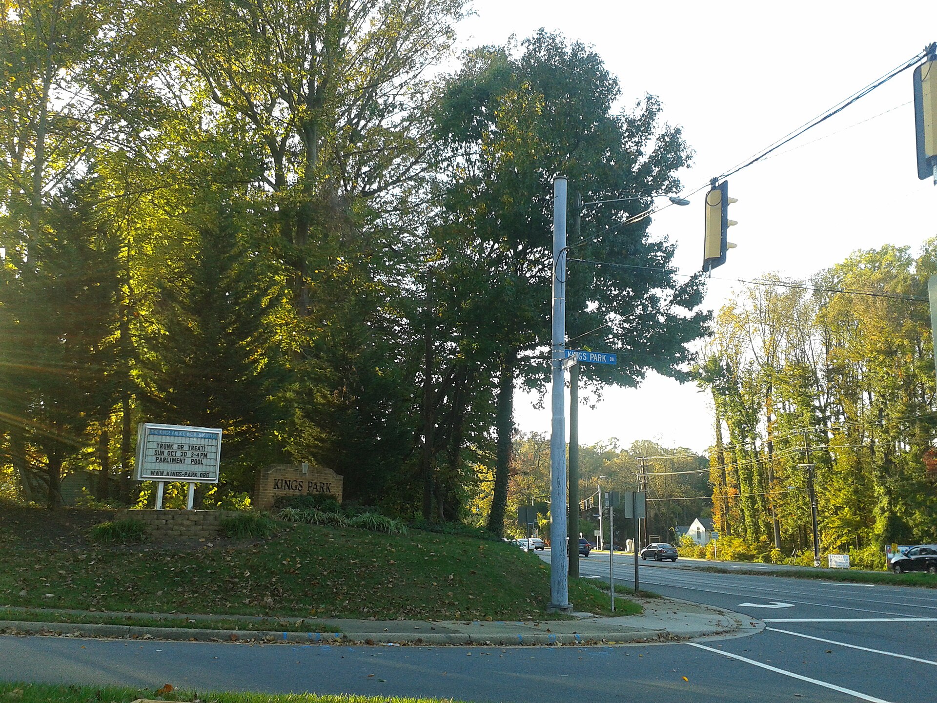 A suburban intersection marking the entrance to Kings Park, Virginia, with trees and a sign.