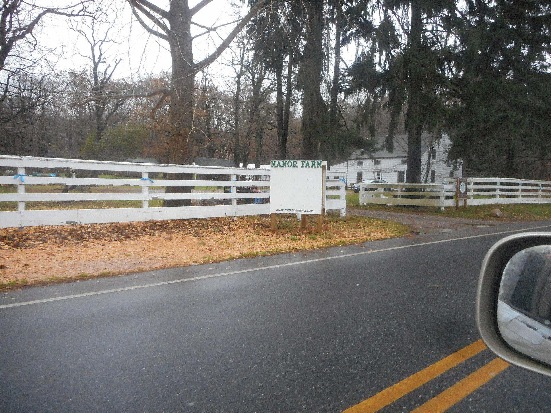 A sign for Manor Farm beside a white fence on Manor Road in Elwood, New York.