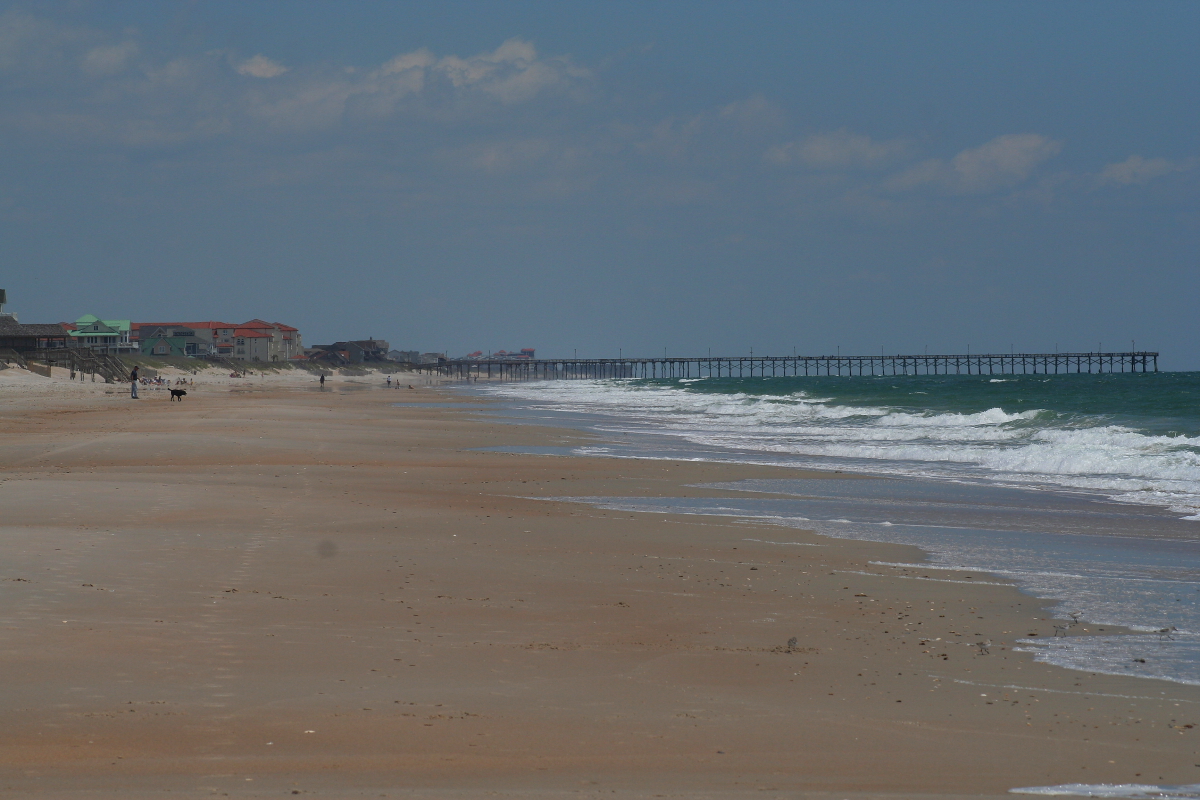 A wide sandy beach at Topsail Island, North Carolina, with a fishing pier.