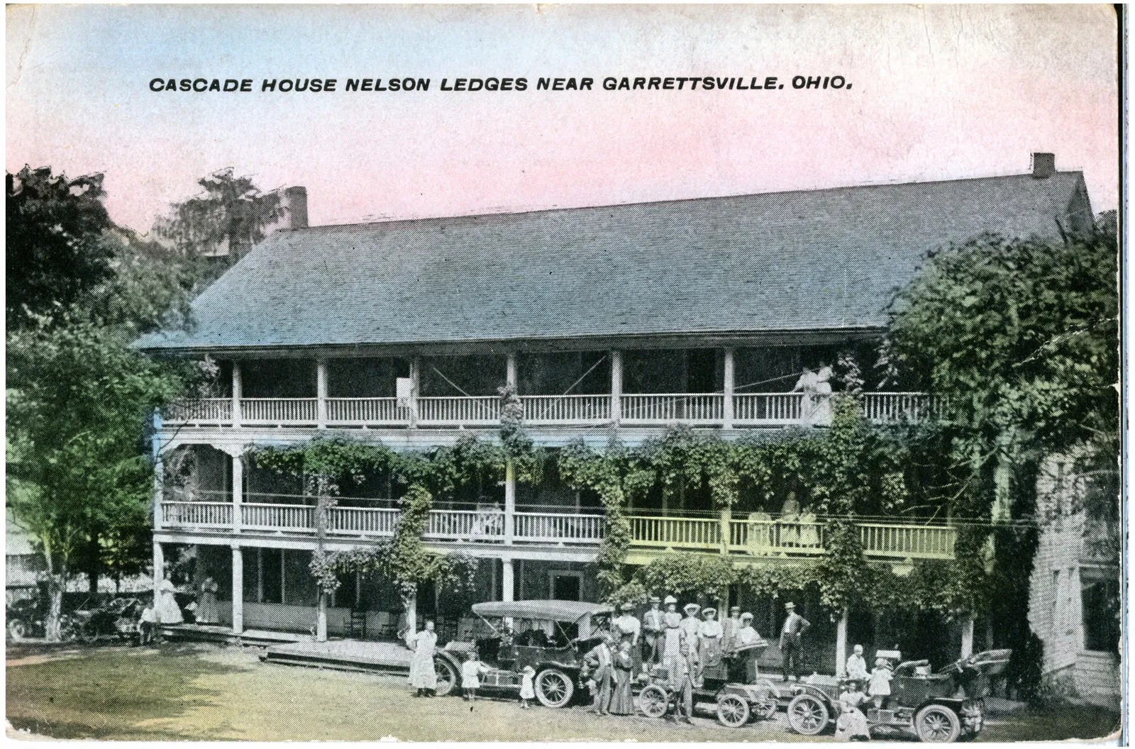 A view of people and cars parked outside of the vine covered hotel.