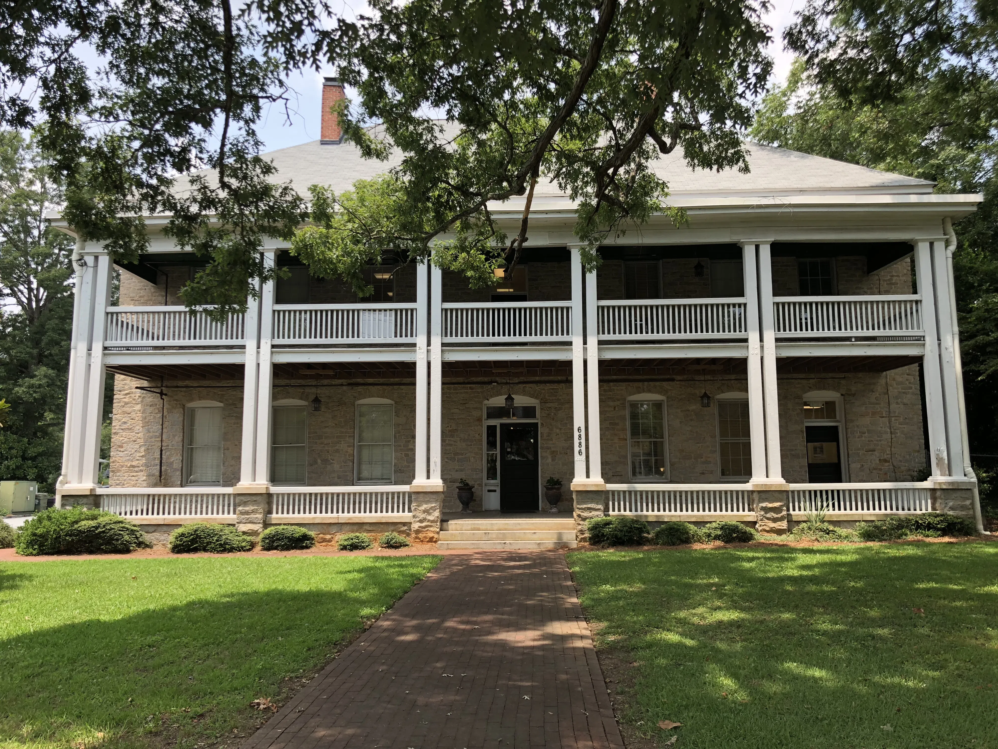 A view from directly in front of the structure, showing the stone facade, two-story veranda, hipped roof and at least one chimney