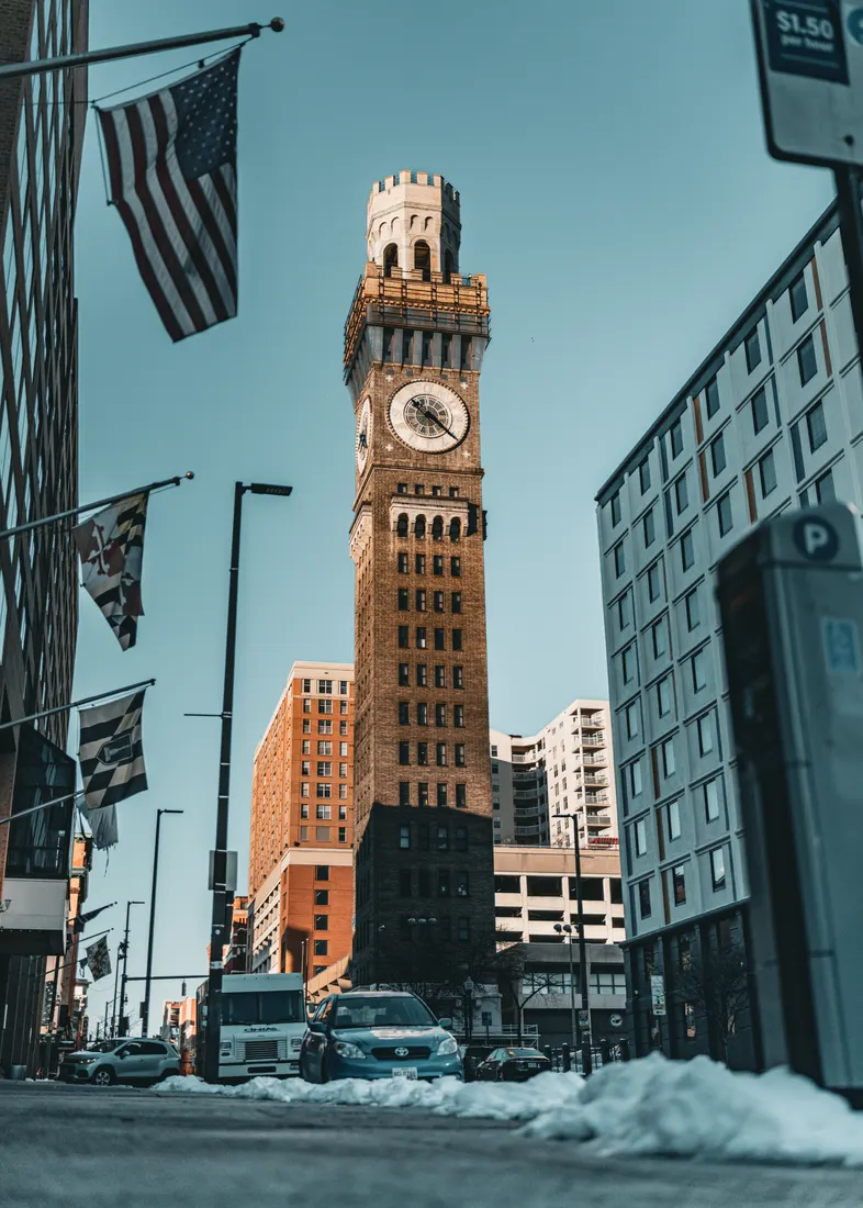 The iconic Bromo-Seltzer Tower in downtown Baltimore, Maryland, framed by urban architecture, snow, and flags. Built in 1911, it remains a historic landmark symbolizing the city's industrial heritage.