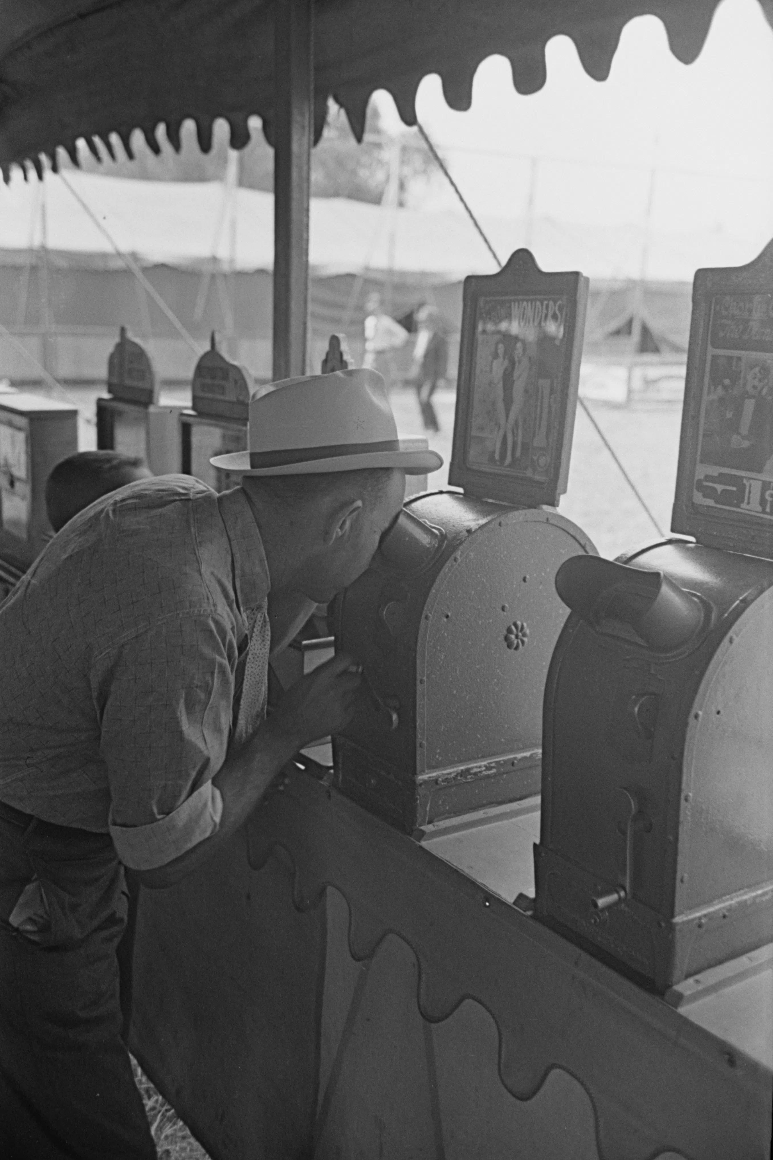 A man looking through a penny peep show at the state fair, Donaldsonville, 1938