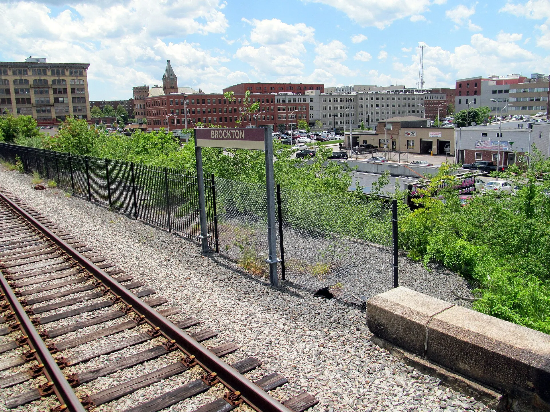 Station sign at Brockton station in June 2017, with the downtown area behind.