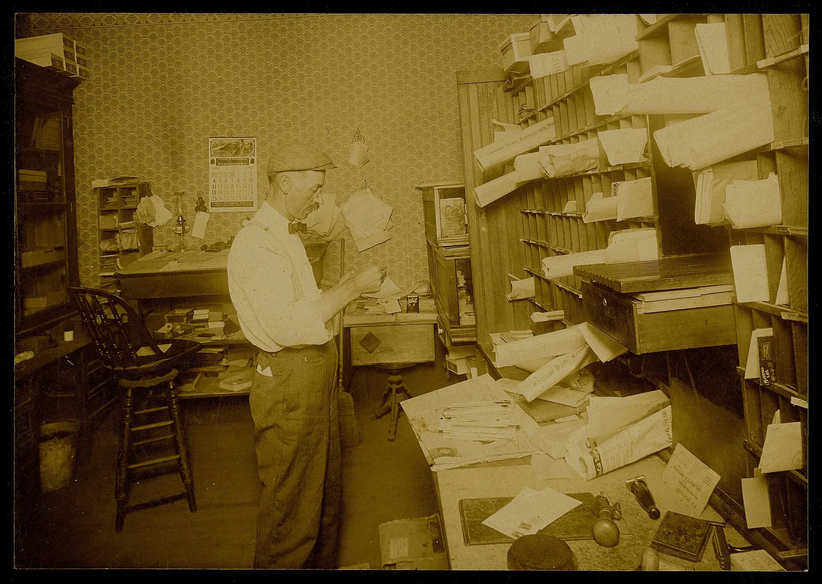 Production Date: 1912 Source Type: Photograph Printer, Publisher, Photographer: Unknown Postmark: Not Applicable Collection: Steven R. Shook Remark: This photograph shows the interior of the Kouts Post Office and Postmaster Charles Henry Wolbrandt at work. The building housing the post office seen h