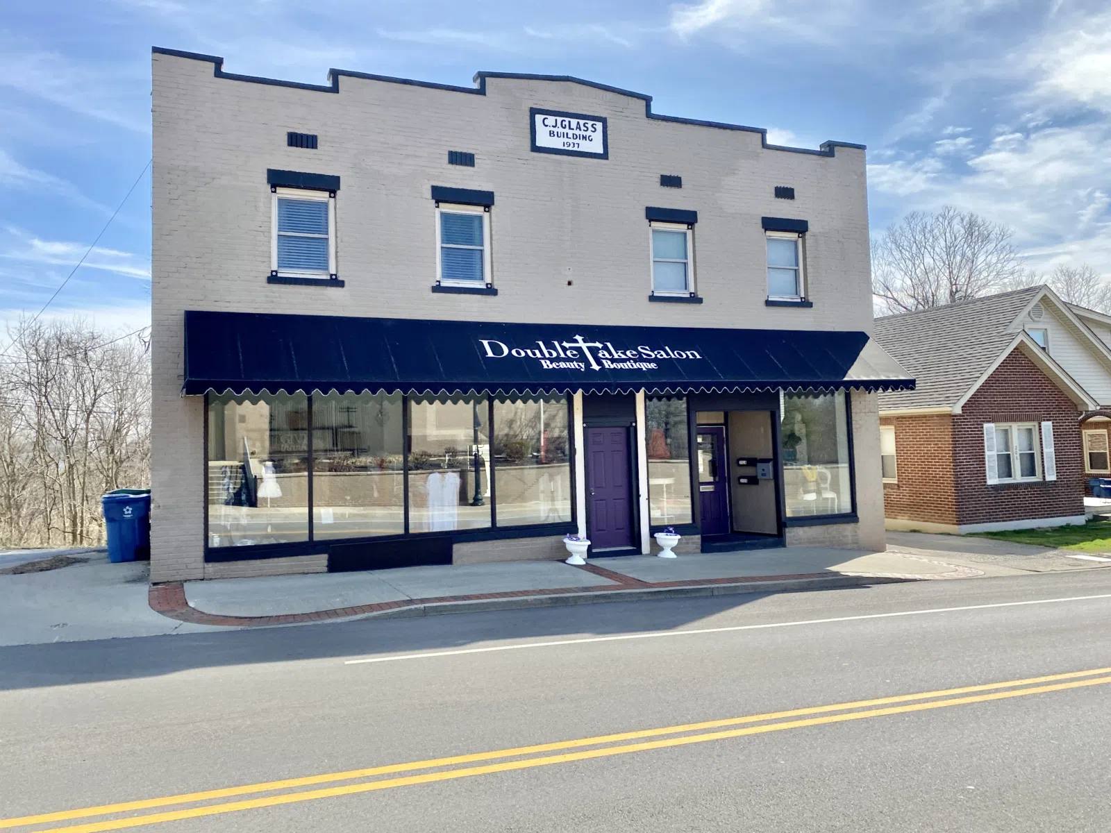 Built in 1937, this commercial building features a painted brick exterior, replacement windows, first floor storefronts, a stepped and gabled parapet with a datestone, and a concrete base.