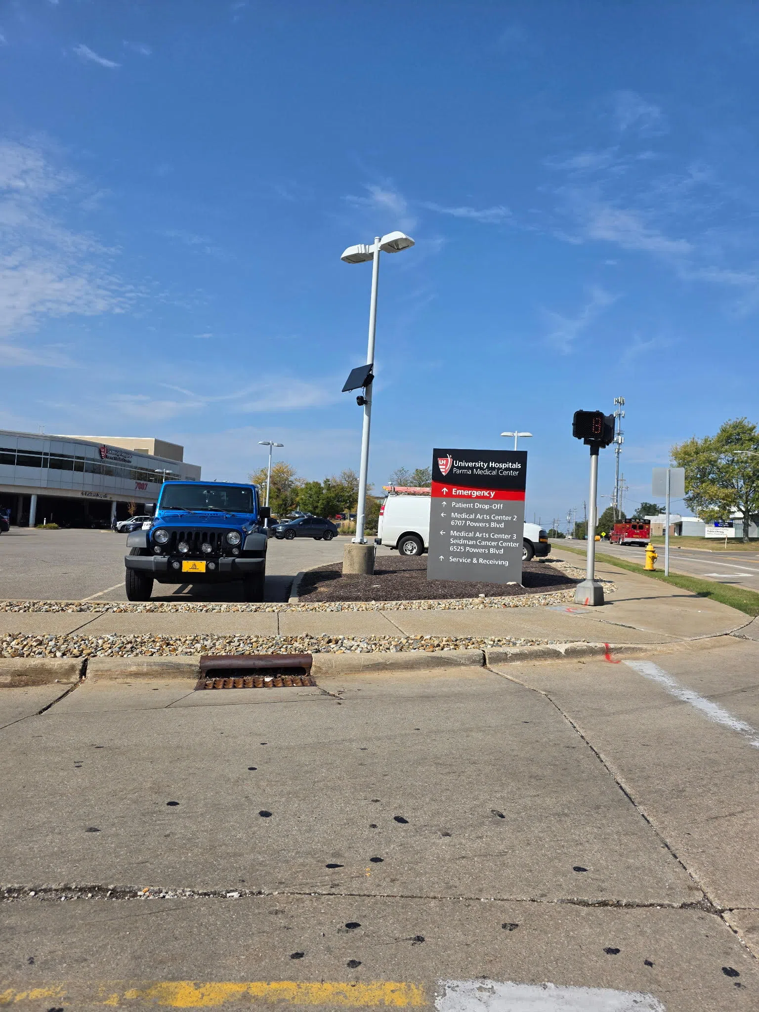 A black license plate reading camera with solar panel above it, attached to a white pole at the entrance to a common parking lot of a local hospital in the greater…