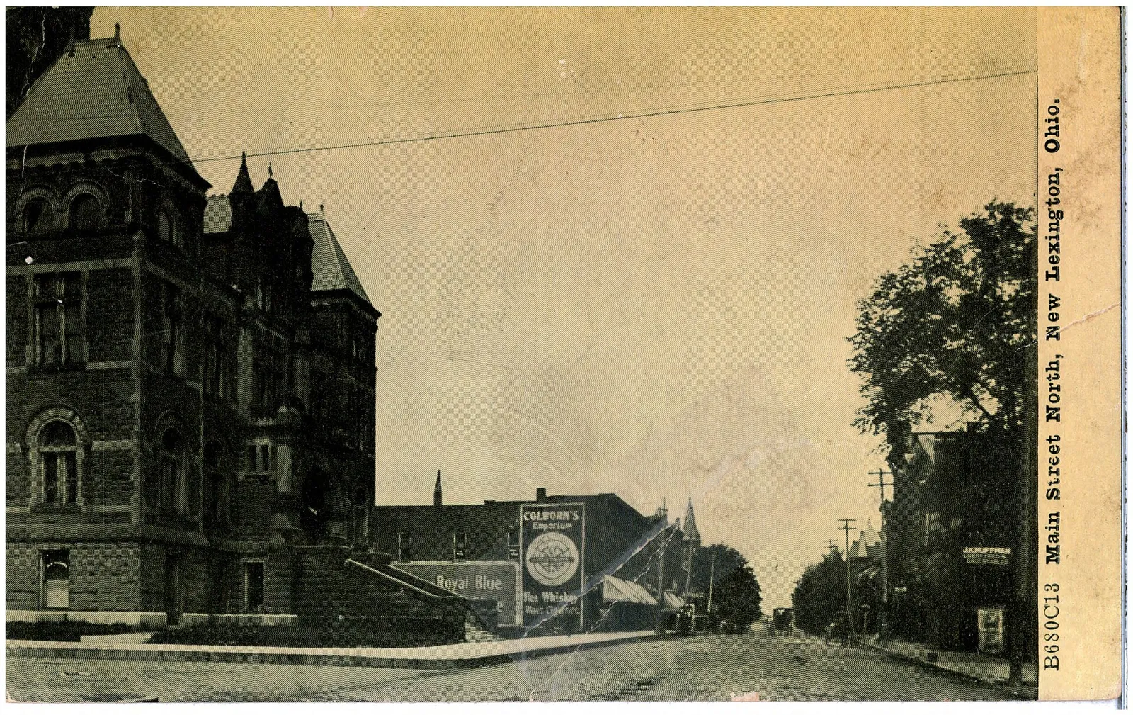 Black and white photograph looking north. What appears to be a court house stands on the corner and a sign advertising Colborn's Emporium next to it. There is a