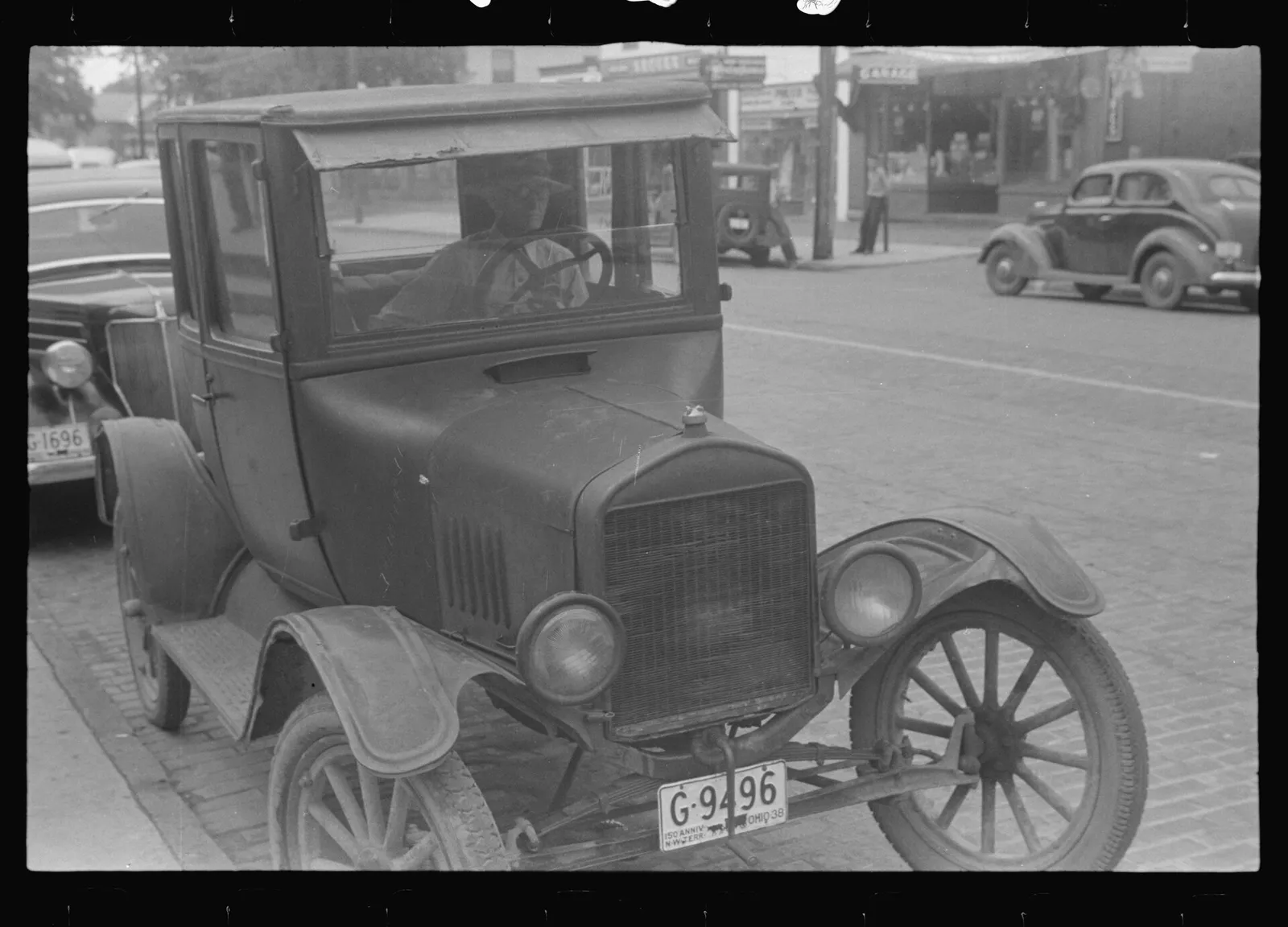 Automobile with crank used to get the motor started, Worthington, Ohio August 1938 Notes: Man seated in Ford Model T, perhaps 20 years old at the time, but look