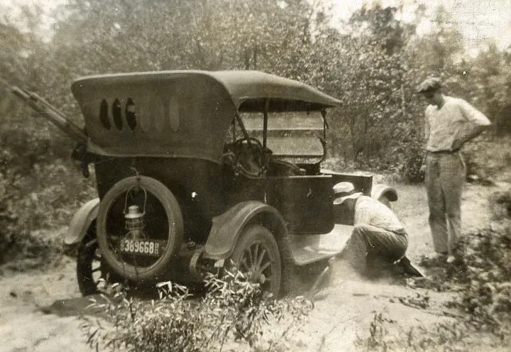 From the Volk Family Collection, a1921 view of two men, Silas Counter and P. G. Volk, as they attempt to dig their stuck car out of the rolling sand on the trail to Harrison, Michigan. Terms associated with the photograp