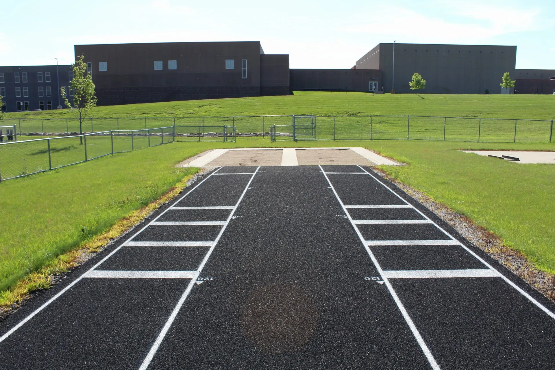 Two parallel outdoor long and triple jump pits with sand trap and school in background. Howard Lake-Waverly-Winsted High School, Minnesota