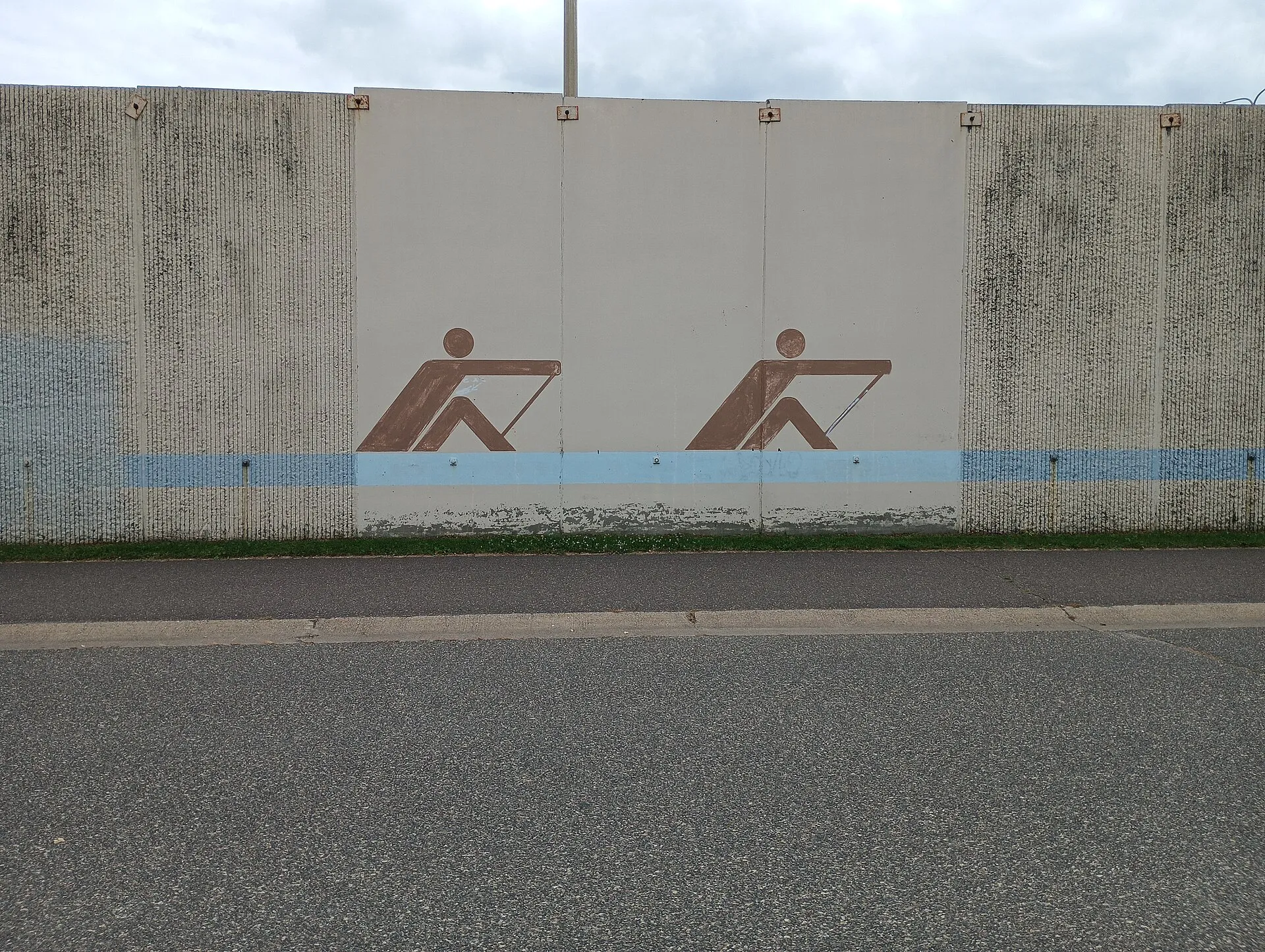 A minimalist mural of two people rowing on the Interstate-694 West retaining wall facing Beach Road and the south side of Long Lake and Long Lake Regional Park, New Brighton, Minnesota. Photo taken by Ulysses Swanson..