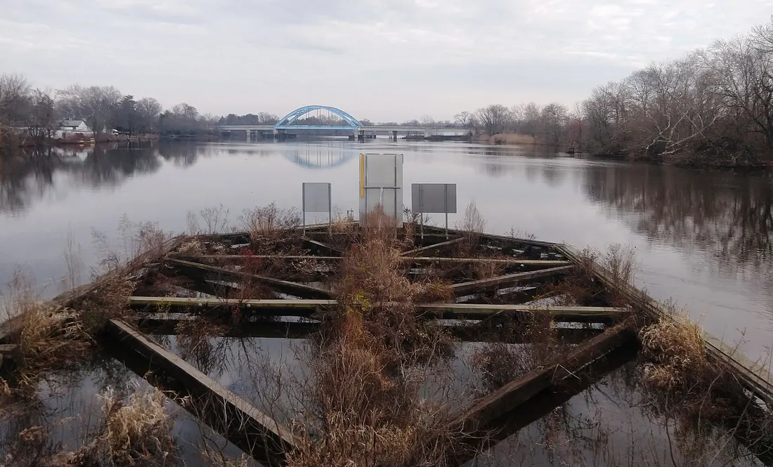 Photo of a wooden pier at the center of the Riverside–Delanco Bridge and the River Line bridge over the Rancocas Creek between Riverside Township (right/south) and Delanco, New Jersey (left/north). Photo taken looking ea