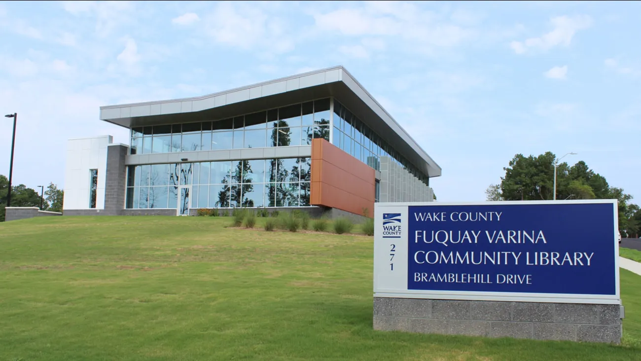A photo of a large library with many glass windows with a visible sign that reads "Fuquay-Varina Community Library"